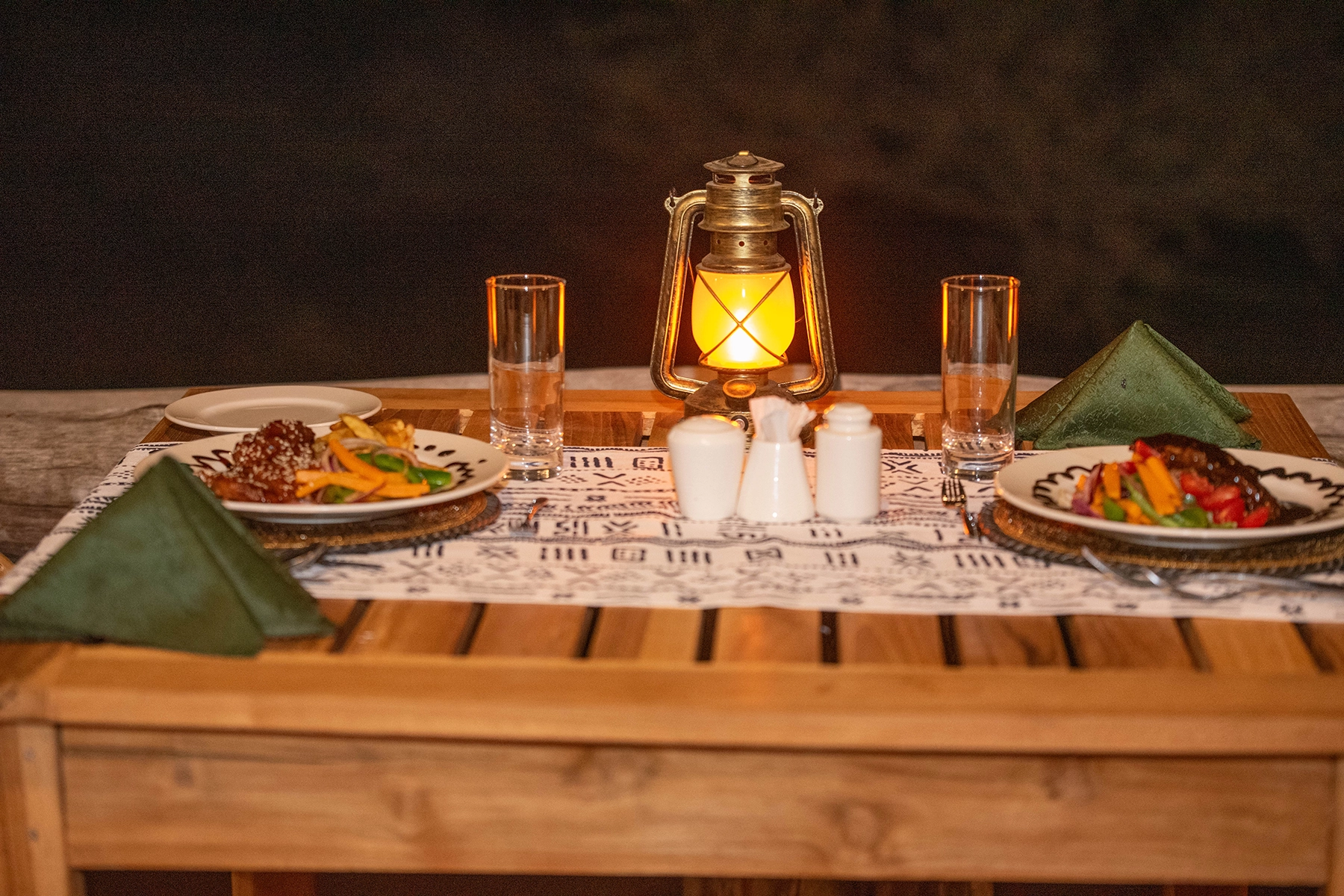 Intimate candlelit dinner for two at Amani Eserian Ngorongoro with a vintage brass lantern, African mudcloth table runner, and plated meals with colourful vegetables