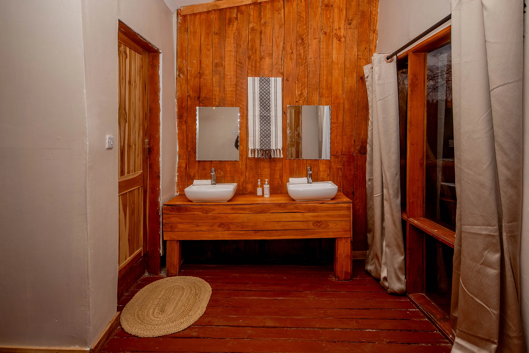 Rustic en-suite bathroom at Amani Eserian Ngorongoro featuring a double vessel sink on a handcrafted wooden vanity with warm timber wall panelling