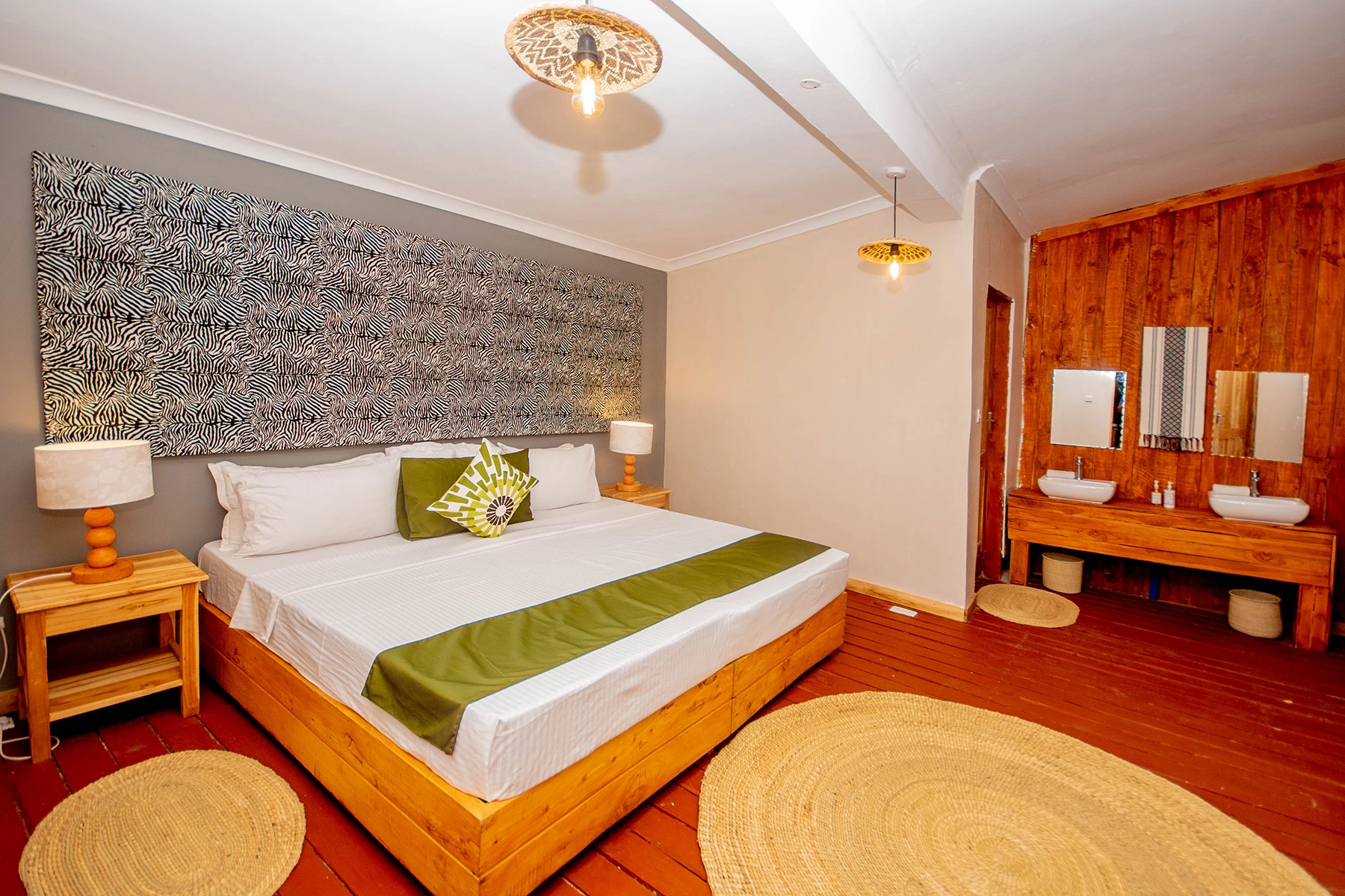 Wide-angle view of king suite at Amani Eserian Ngorongoro showing zebra-print feature wall, green accent bedding, timber floors, and open-plan en-suite vanity