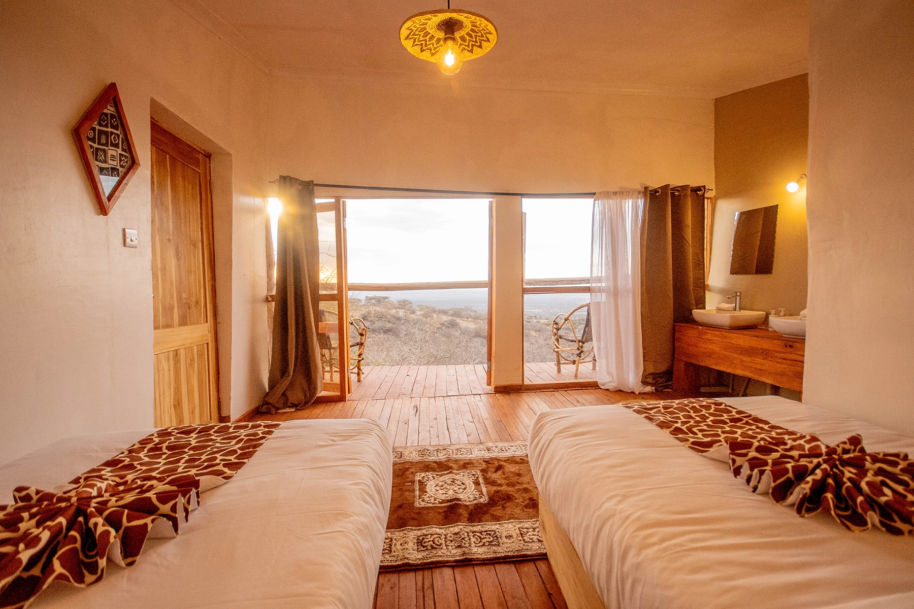 Bright twin room at Amani Eserian Ngorongoro with giraffe-print bedding, open balcony doors, and sweeping views over the Ngorongoro highlands