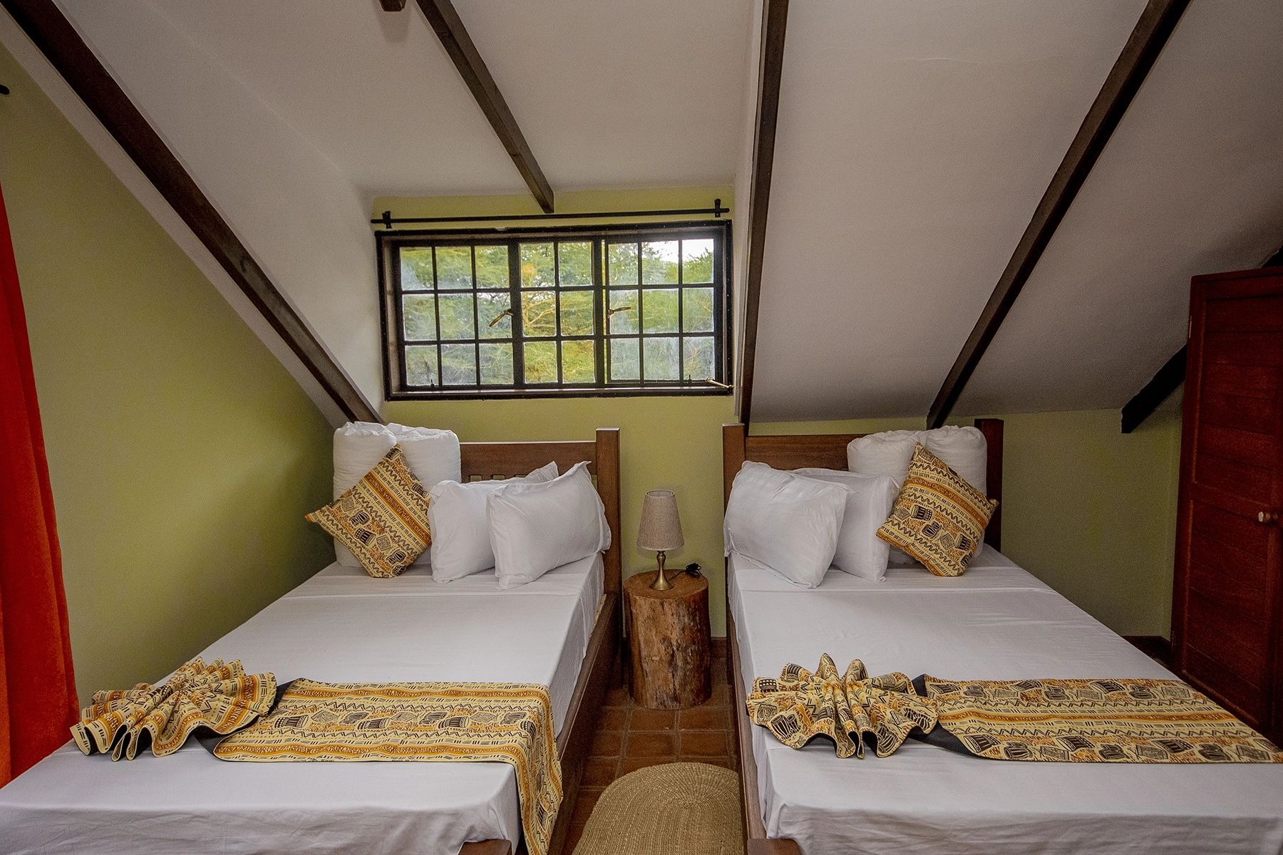 Cosy attic twin room at Amani Farmhouse Tanzania with sloped beam ceiling, two wooden single beds with African-print runners, and a garden-view window