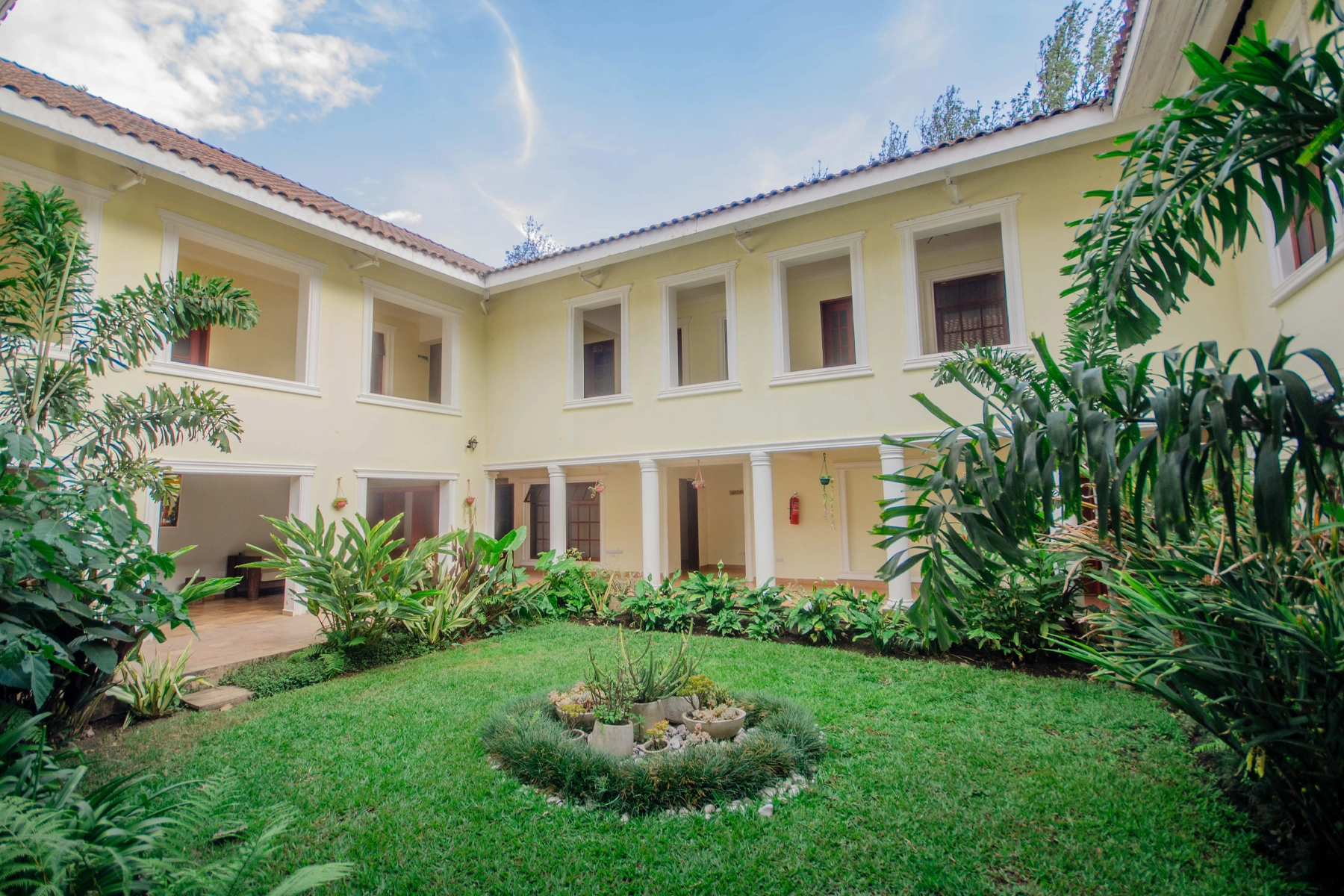 Lush inner courtyard garden at Amani Safari Lodge Tanzania with a circular succulent planter on the lawn, surrounded by the lodge's two-storey yellow L-shaped wing and tropical plants