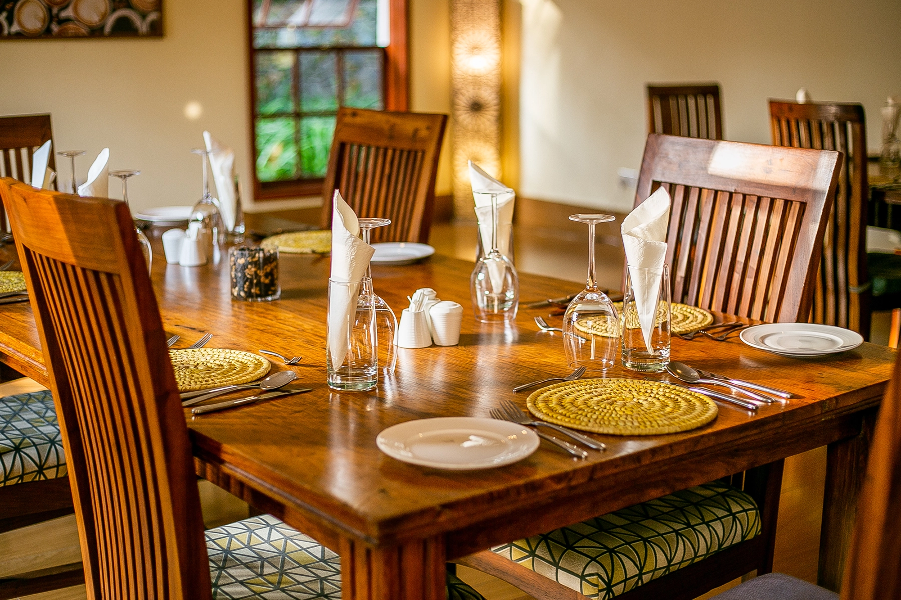 Elegantly set hardwood dining table at Amani Safari Lodge Tanzania restaurant with woven placemats, folded napkins, and wine glasses