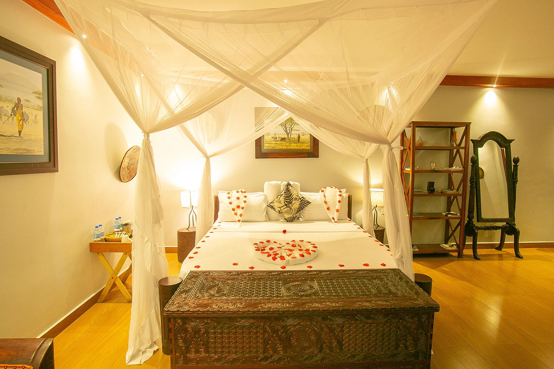 Romantic four-poster canopy bed at Amani Safari Lodge Tanzania decorated with a heart-shaped rose petal arrangement, soft lighting, and carved wooden chest
