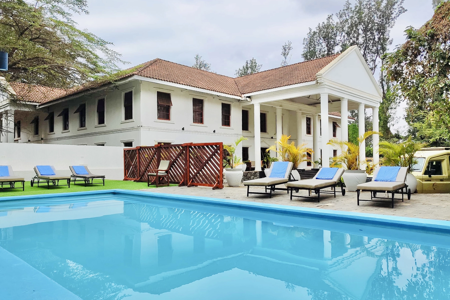 Outdoor swimming pool with sun loungers at Amani Safari Lodge Tanzania with the colonial white lodge building in the background