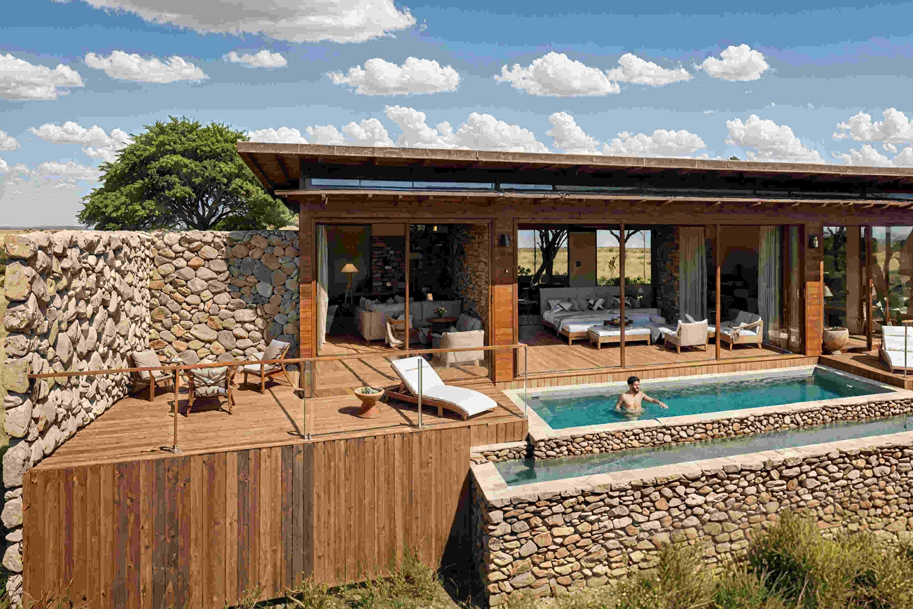 Architectural render of a luxury safari villa exterior at The Bomas by Amani Collection Lobo Serengeti, showcasing a stone and timber faÃ§ade, open-plan living area with glass sliding doors, a private lap pool, and a sun deck overlooking the open Serengeti grasslands